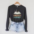 Unearth A Story Skeleton Dinosaur Book Summer Reading 2026 Raglan Sleeve Sweatshirt Dark Grey Heather Unearth A Story Skeleton Dinosaur Book Summer Reading 2026 Raglan Sleeve Sweatshirt Dark Grey Heather