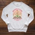 Unearth a Story 2026 Summer Reading Program Flowers Book Raglan Sleeve Sweatshirt Heather Mustard