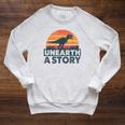 Unearth A Story Dinosaur Reader Book Lover 2026 Raglan Sleeve Sweatshirt Heather Mustard