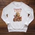 Women's Unearth a Story Triceratops Dinosaur Reading Books Dino Raglan Sleeve Sweatshirt Heather Mustard