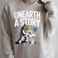 Unearth A Story Astronaut Finds Book On The Moon Raglan Sleeve Sweatshirt Heather Forest