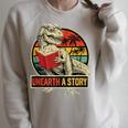 Unearth a Story Dinosaur Reading Book Dino T Rex Summer 2026 Raglan Sleeve Sweatshirt Heather Forest