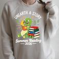 Unearth a Story Triceratops Dinosaur Reading Books Cute Dino Premium Tri-Blend Raglan Sleeve Sweatshirt Heather Forest