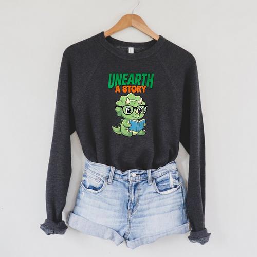 Women's Unearth a Story Summer Reading 2026 Triceratops Dino Book Raglan Sleeve Sweatshirt - Bookorys