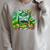Unearth a Story Library Summer Reading 2026 Dinosaur Book Raglan Sleeve Sweatshirt Heather Forest