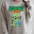 Women's Unearth a Story Summer Reading 2026 Triceratops Dino Book Raglan Sleeve Sweatshirt Heather Forest