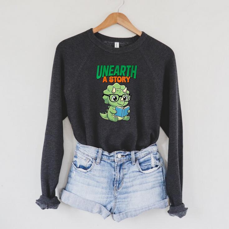 Women's Unearth a Story Summer Reading 2026 Triceratops Dino Book Raglan Sleeve Sweatshirt